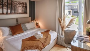 A modern bedroom with a large bed, a side table, a glass table, and a view of a building through the window. - Hôtel à la maison - Luxe Alpine MSA (Beaupré)