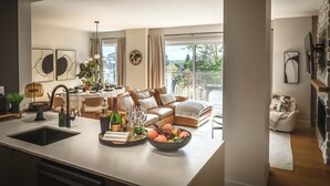 A modern living room with a sofa, dining area, and a large window with a view. - Hôtel à la maison - Luxe Alpine MSA (Beaupré)