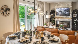 A dining area with a round table set for six, a stone fireplace, and a world map wall decoration. - Hôtel à la maison - Luxe Alpine MSA (Beaupré)