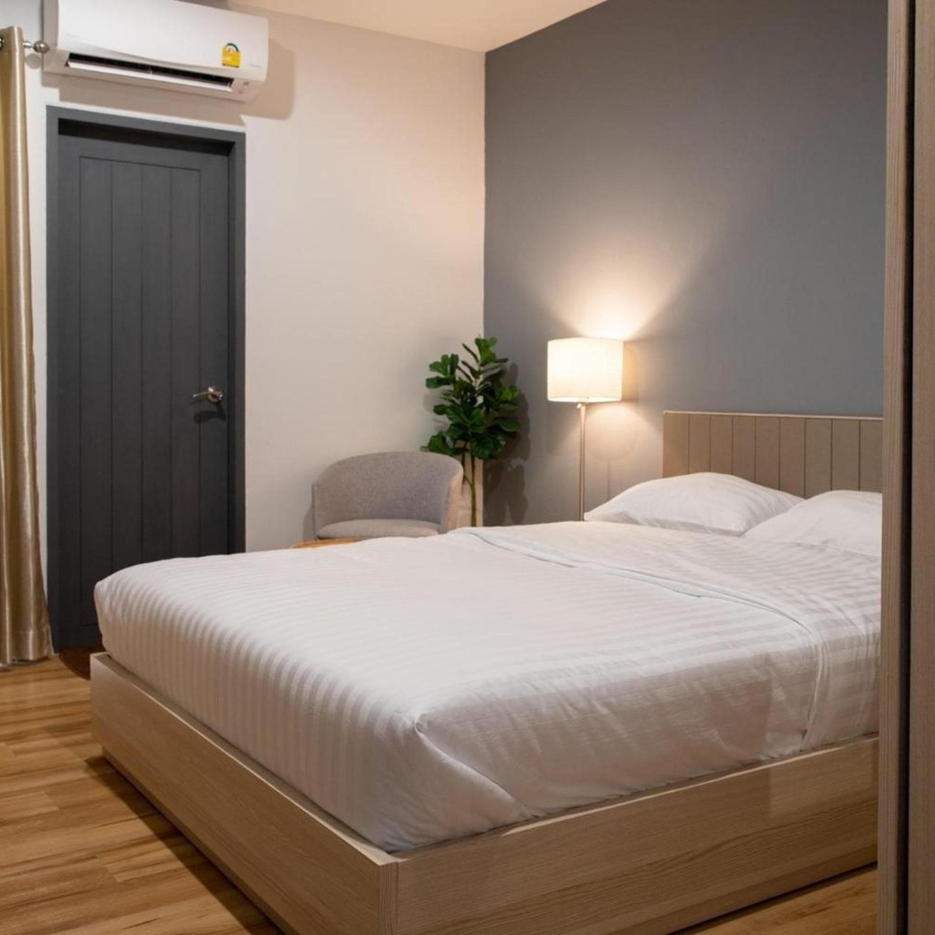 A bedroom with a bed, a nightstand, a lamp, a potted plant, and an air conditioning unit.