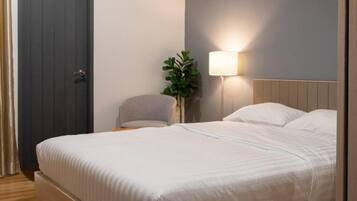 A bedroom with a bed, a nightstand, a lamp, a potted plant, and an air conditioning unit.