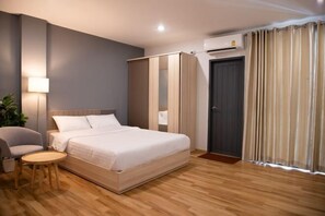 A modern hotel room with a bed, a chair, a small table, a wardrobe, and a door with curtains. - J & L Residence and Spa (Bangkok)