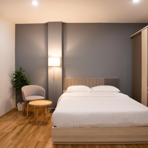 Una habitación de hotel con cama, una silla, una mesita, una lámpara y una planta en maceta.