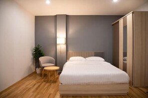 A modern bedroom with a large bed, a chair, a small table, a lamp, and a plant. - J & L Residence and Spa (Bangkok)