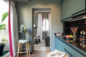 Une cuisine moderne avec des meubles de couleur sombre, un plan de travail noir et une fenêtre agrémentée de rideaux blancs.
