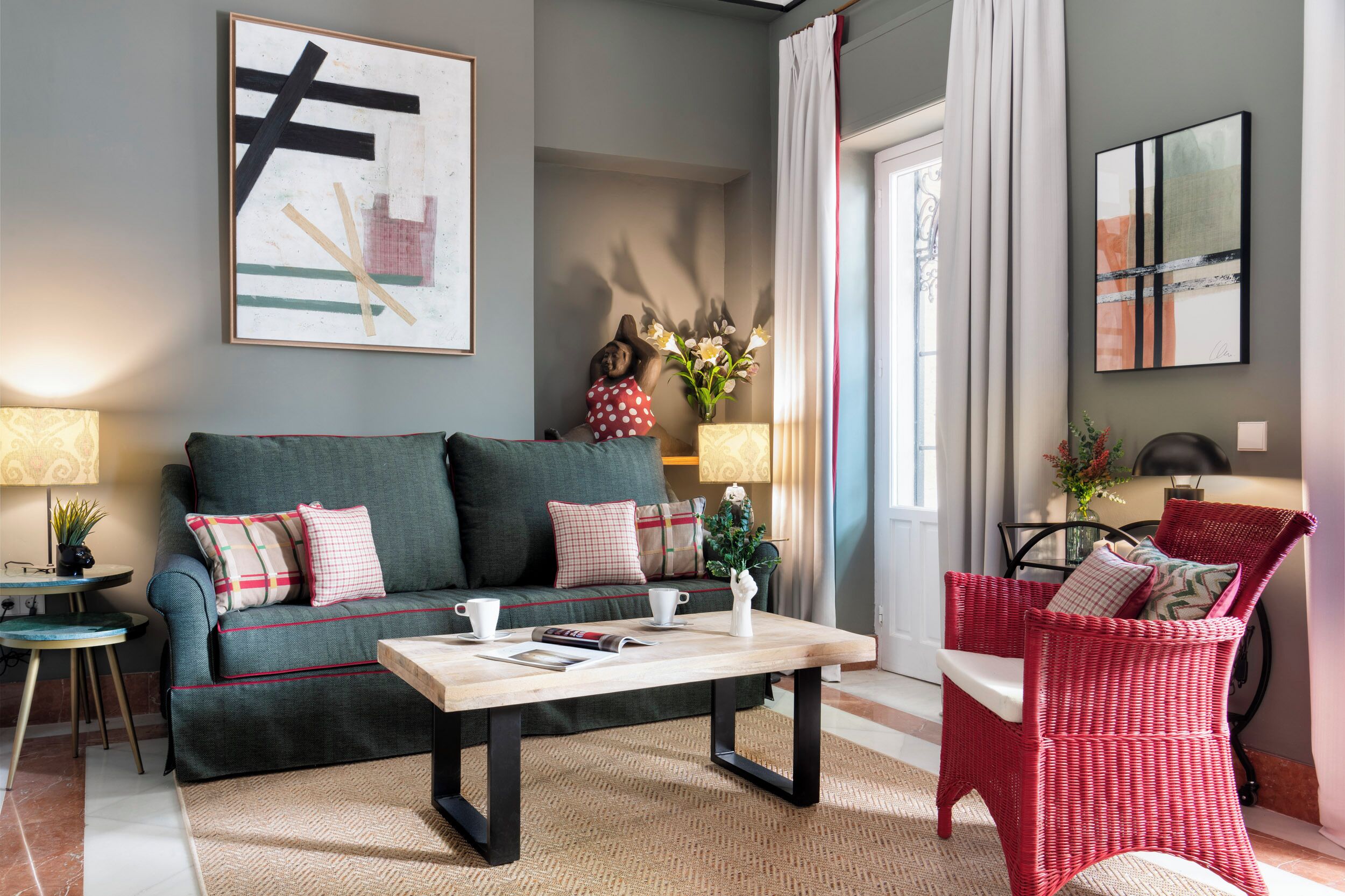Un salon comprenant un canapé, une table basse, un fauteuil en osier rouge et des œuvres d’art accrochées aux murs.