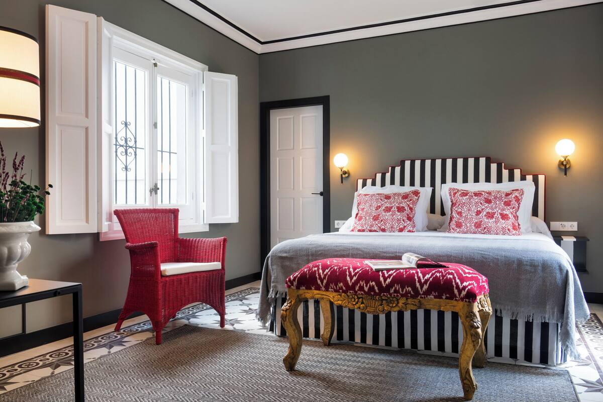 A bedroom with a bed, a red chair, a bench, and a door.
