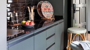 Une cuisine moderne avec des meubles gris, un pare-feu noir et un four à micro-ondes. On y trouve des tabourets en bois et une assiette décorée posée sur le comptoir.