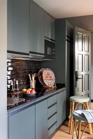 A modern kitchen with grey cabinets, a black backsplash, and a microwave. There are wooden stools and a patterned plate on the counter. - CSE Puerta de Armas Apartments (Seville)