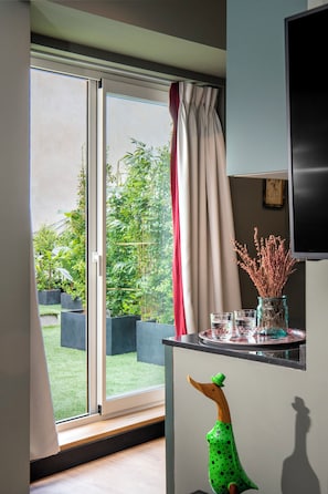 Una habitación con puerta corrediza de vidrio que da a un jardín, una mesita con un florero y vasos, y una escultura decorativa de pato.