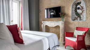 Une chambre à coucher avec un lit, un fauteuil en osier rouge, une cheminée et un téléviseur fixé au mur.