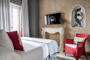 Un dormitorio con cama, una silla de mimbre roja, chimenea y televisor montado en la pared.