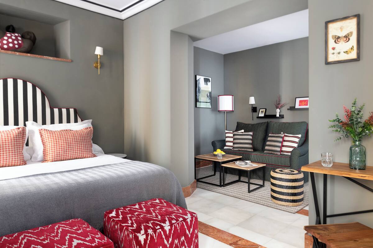 A modern hotel room with a large bed, a sofa, a small table, and a side table.