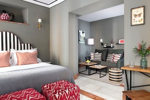 A modern hotel room with a large bed, a sofa, a small table, and a side table. - CSE Puerta de Armas Apartments (Seville)