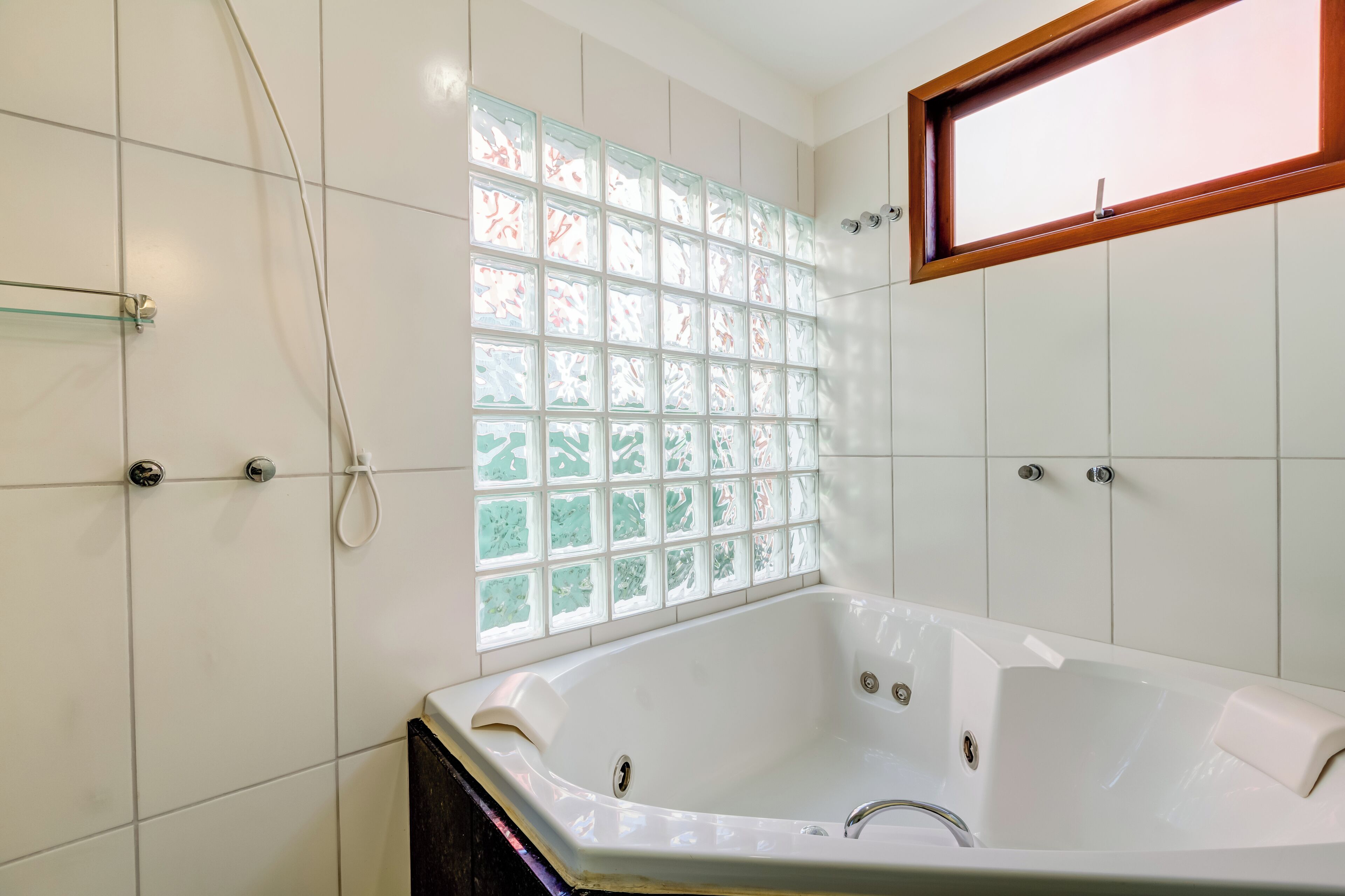 Een badkamer met een groot bad, een raam met gezandstraald glas en witte betegelde muren.