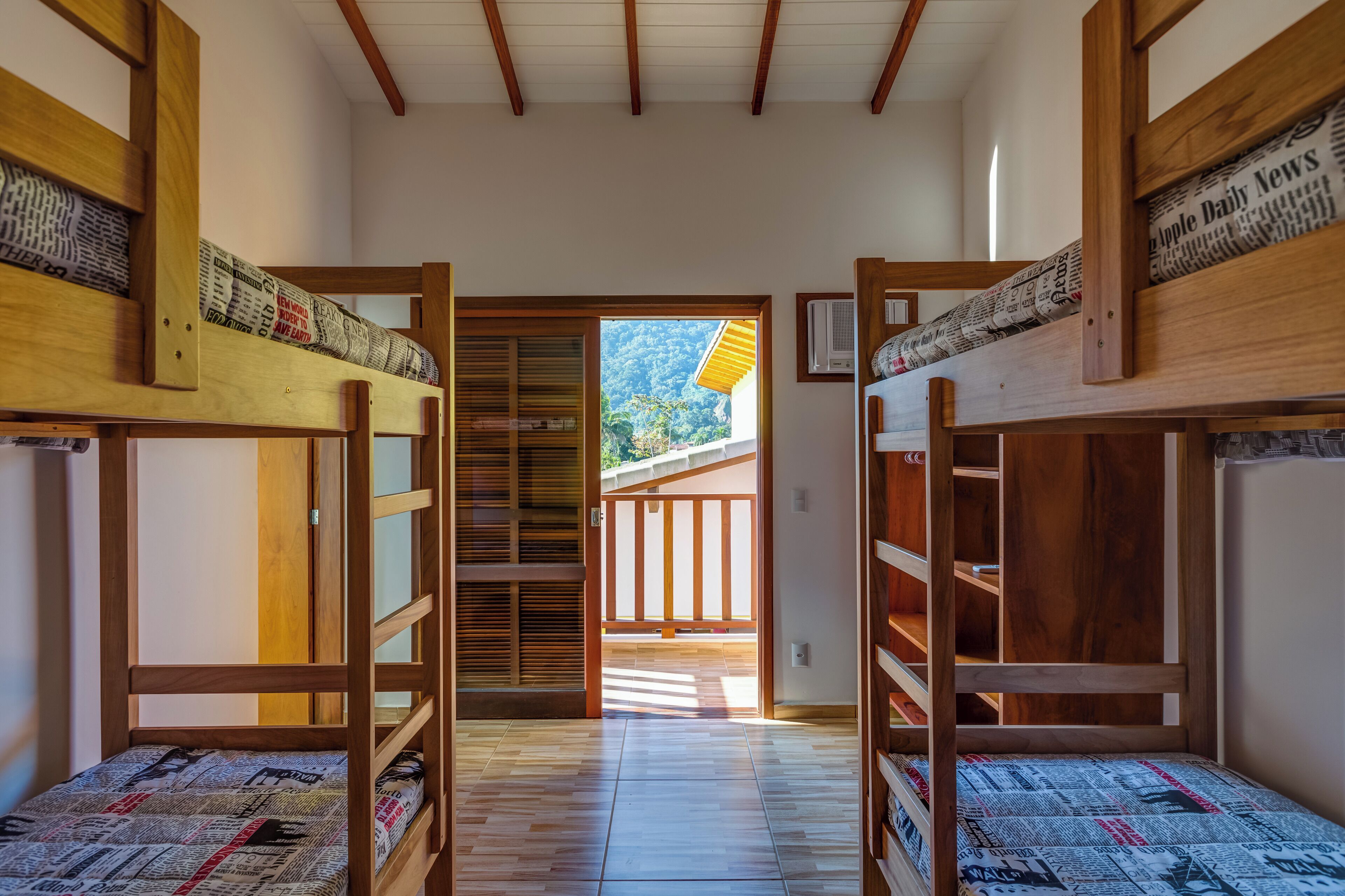 A room with bunk beds, a wooden floor, and a view of a balcony with a wooden railing.