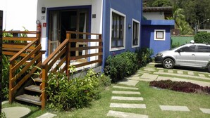 Un edificio de dos pisos con fachada azul, una escalera de madera y un coche estacionado adelante.