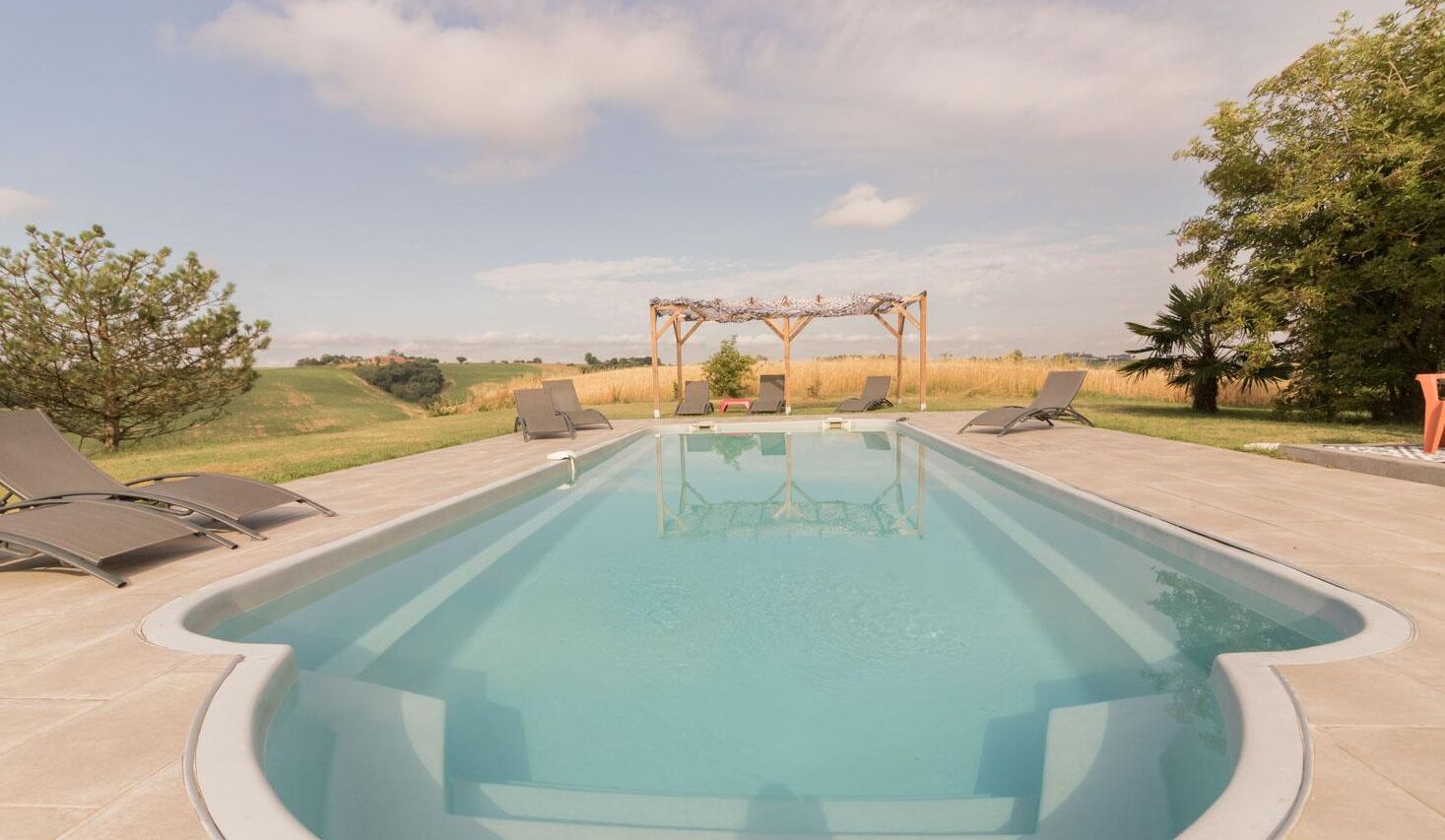 Una piscina rectangular con sillones de descanso y una pérgola.