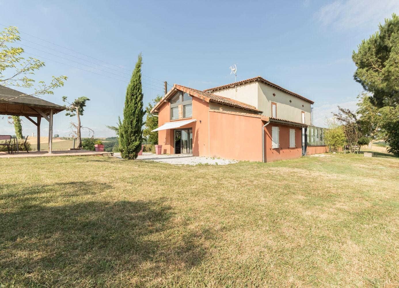 A two-story house with a tiled roof, a covered patio, and a grassy yard.