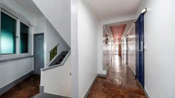 Un largo pasillo estrecho con una escalera a la izquierda, una puerta azul a la derecha y un techo rojo.