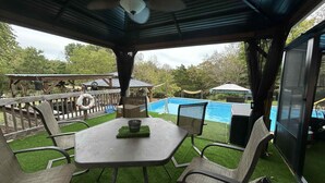 An outdoor patio with a table and chairs, a pool, and a covered area with a ceiling fan.