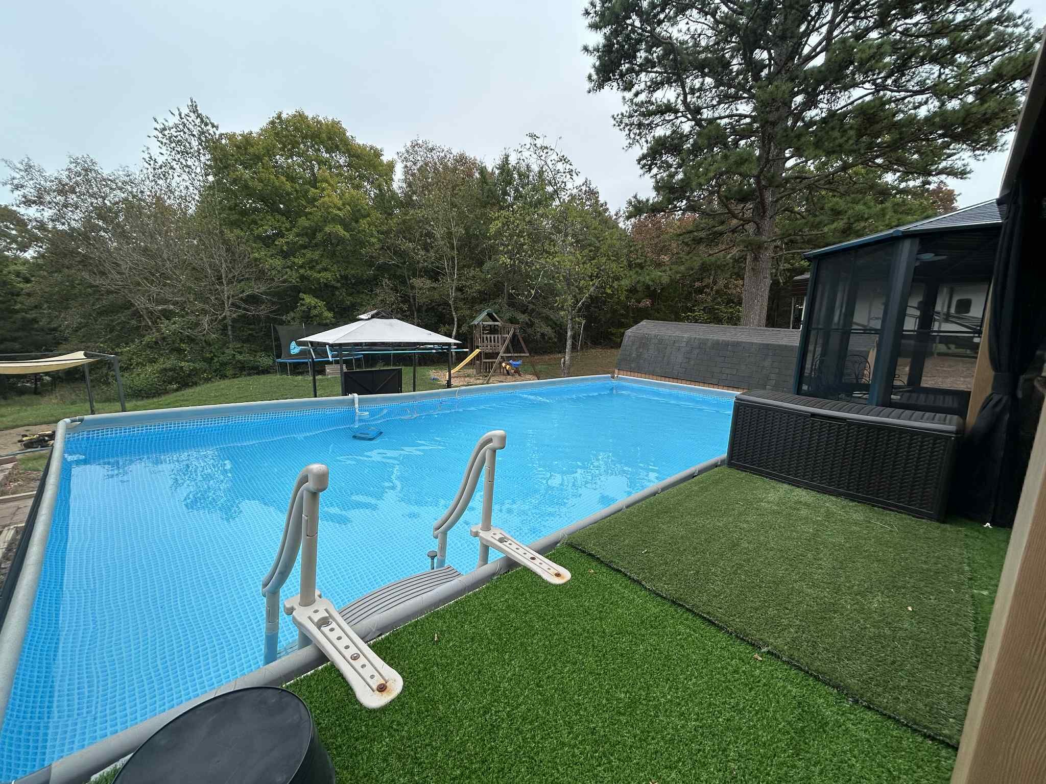A swimming pool with steps leading into it, surrounded by artificial grass and trees.