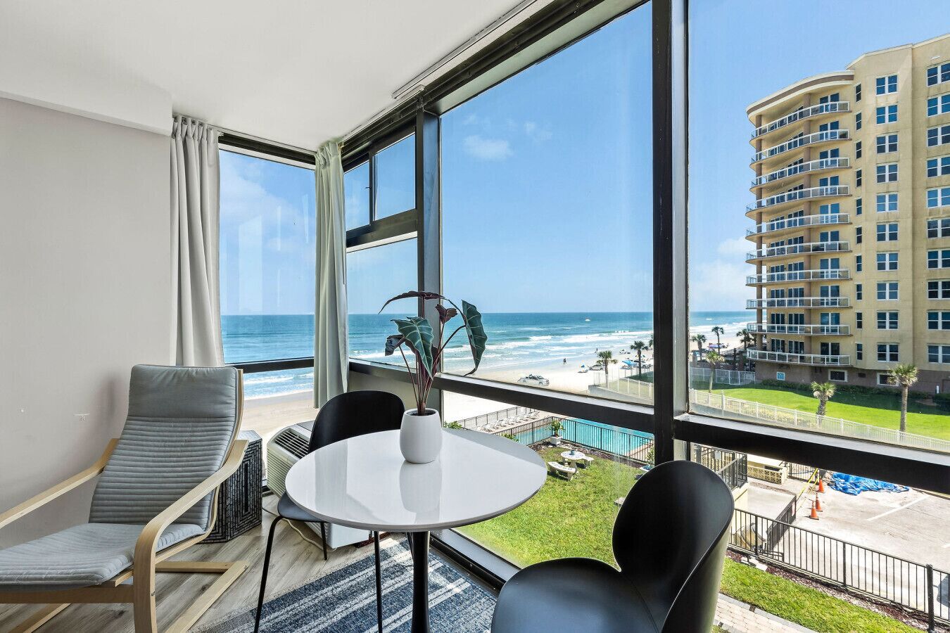 A hotel room with a large window overlooking a beach and a high-rise building.