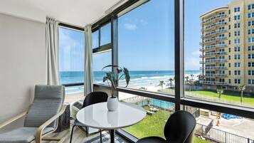 A hotel room with a large window overlooking a beach and a high-rise building.