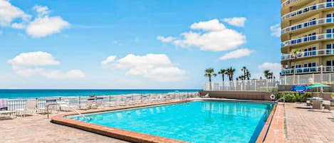 A swimming pool with a view of the ocean, surrounded by lounge chairs and a tall building.