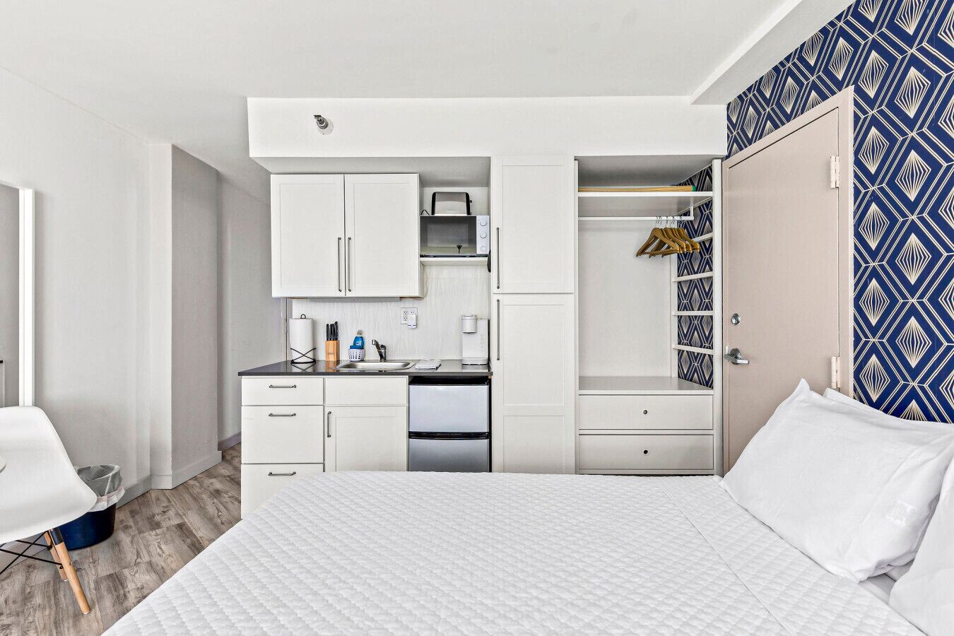 A compact bedroom with a bed, a small kitchenette, and a wardrobe.