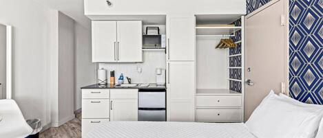 A compact bedroom with a bed, a small kitchenette, and a wardrobe.