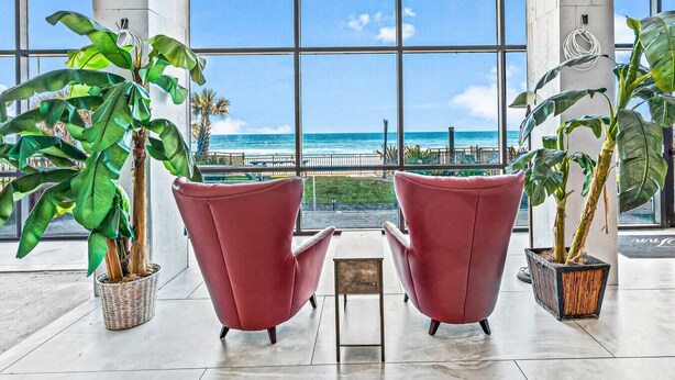 A spacious room with large windows offering a view of the ocean and a beach. There are two red chairs and potted plants. - Modern Studio with 2 Queen Beds | Partial Ocean View | Pool & Beach Access (Daytona Beach)