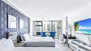 A modern hotel room with a large bed, a desk, a TV, and a view of a cityscape through large windows. - Modern Studio with 2 Queen Beds | Partial Ocean View | Pool & Beach Access (Daytona Beach)