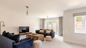 A modern living room with a TV, sofas, ottomans, and a coffee table.
