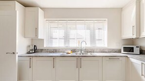 A modern kitchen with white cabinets, a sink, a microwave, and a window with blinds.