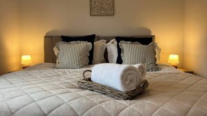 A neatly made bed with a quilted duvet, striped pillows, and a rolled towel on a woven basket.