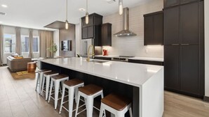 Una cocina moderna con una isla grande, taburetes de bar, armarios oscuros e iluminación colgante.