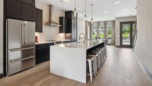 Cocina moderna con armarios oscuros, electrodomésticos de acero inoxidable y una isla central con taburetes de bar.