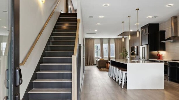 Una cocina moderna con una isla central, una escalera y un comedor.