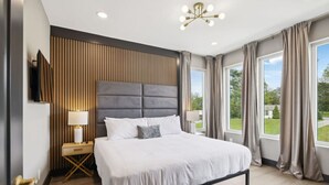 Een moderne hotelkamer met een groot bed, een wand van houten panelen, een aan de muur bevestigde televisie en uitzicht op het omliggende landschap door de ramen.