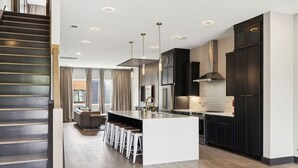 Een moderne keuken met een centraal eiland, donkere kastjes en een trap naar een ander niveau.