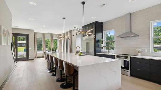 A modern kitchen with a large island, bar stools, stainless steel appliances, and a view of the outdoors. - Stunning 4 Bedroom/ 4.5 Bath Home w/Rooftop Deck! (Nashville)