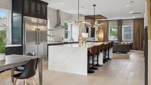A modern kitchen with a central island, dark cabinetry, stainless steel appliances, and a dining area with a table and chairs. - Stunning 4 Bedroom/ 4.5 Bath Home w/Rooftop Deck! (Nashville)