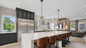 A modern kitchen with a large island, dark cabinetry, stainless steel appliances, and a bar area with stools. - Stunning 4 Bedroom/ 4.5 Bath Home w/Rooftop Deck! (Nashville)