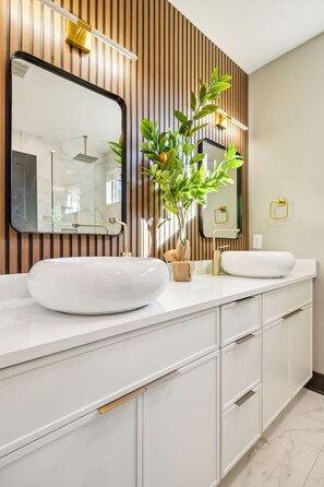 A modern bathroom with two white sinks, a large mirror, and a wooden panel wall.