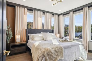 A modern bedroom with a large bed, a bedside table, a nightstand, and a window with curtains.