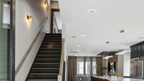 Una cocina moderna con una isla central, una escalera y un comedor con taburetes de bar.