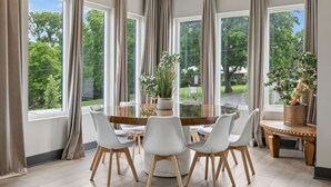 Un comedor con una mesa redonda, sillas blancas y vistas a zonas verdes.