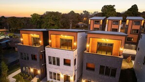 A modern multi-story residential building with a flat roof, large windows, and a well-lit entrance.