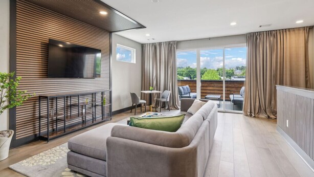 A modern living room with a sofa, TV, and a balcony with outdoor seating.